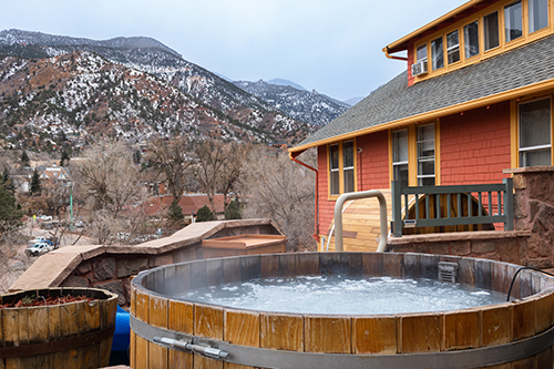 Wooden barrel hot tub on the deck of a rustic lodge with a view of snow-dusted mountains